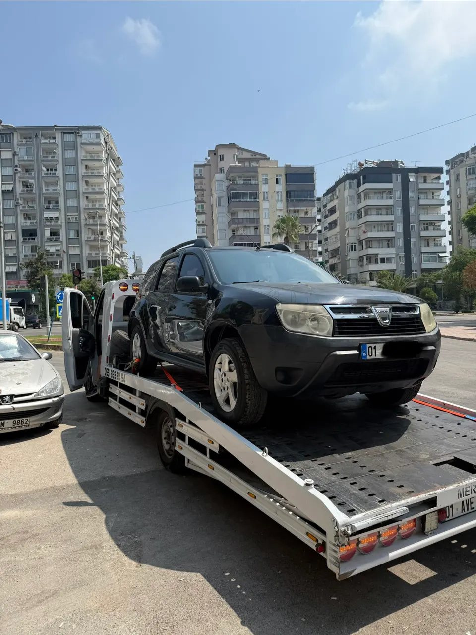 Siyah Dacia Duster kayar kasalı çekiciye yüklenmiş, şehir içinde apartmanların önünde